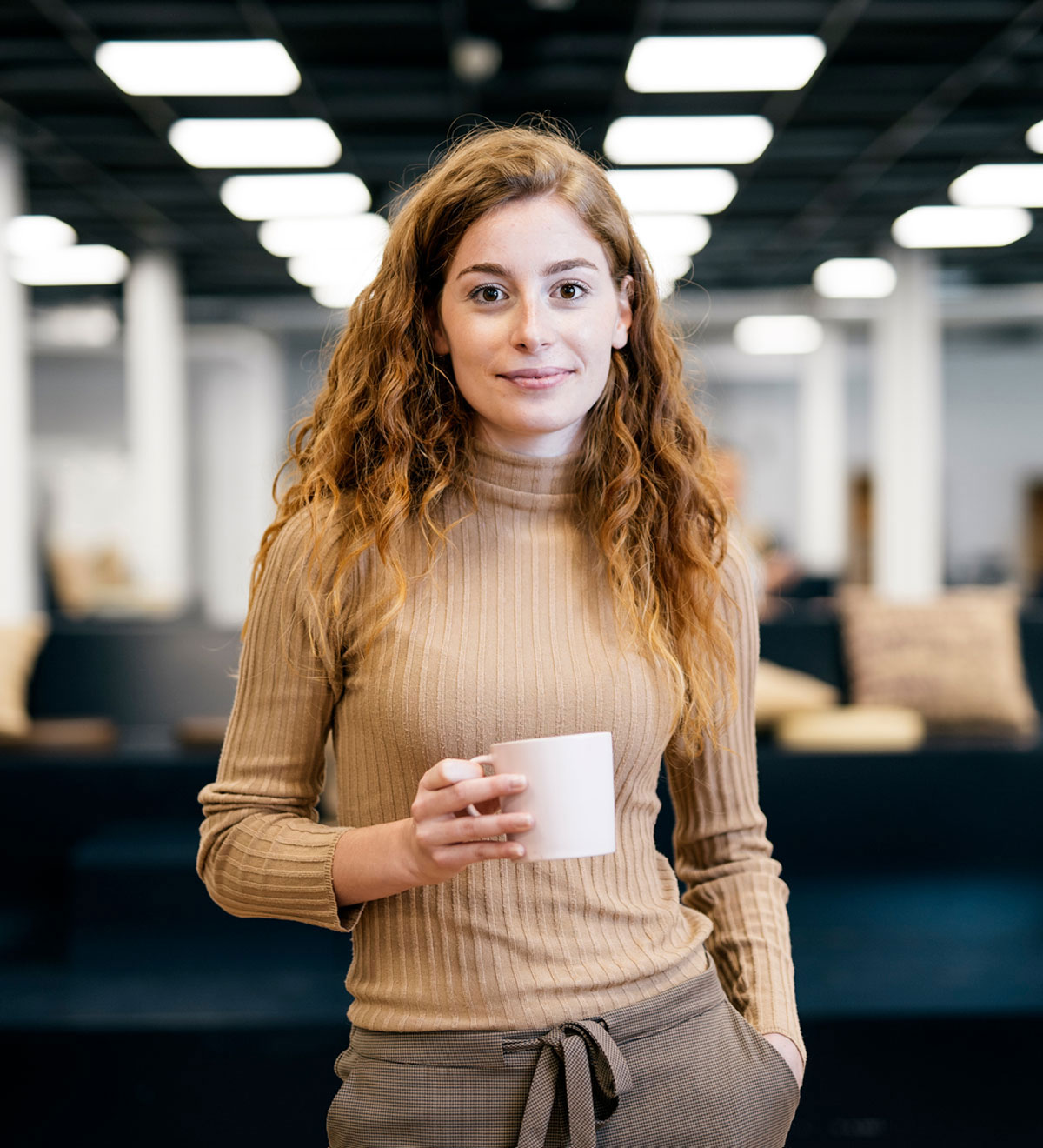 Red-haired woman standing with coffee cup in an office